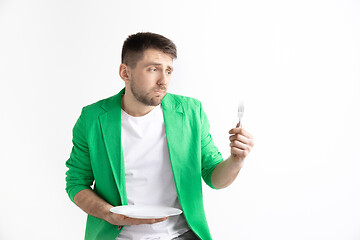 Image showing Young sad attractive guy holding empty dish and fork isolated on grey background.