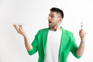 Image showing Young smiling attractive guy holding empty dish and fork isolated on grey background.