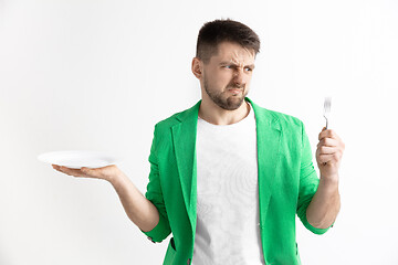 Image showing Young sad attractive guy holding empty dish and fork isolated on grey background.