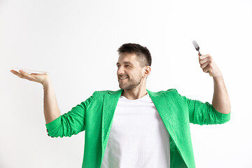 Image showing Young smiling attractive guy holding empty dish and fork isolated on grey background.