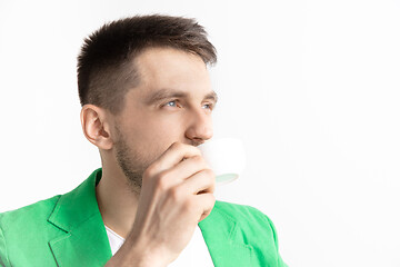 Image showing Taking a coffee break. Handsome young man holding coffee cup, smiling while standing against gray background