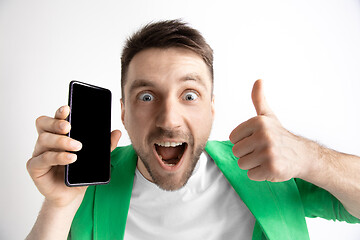 Image showing Young handsome man showing smartphone screen and signing OK isolated on gray background