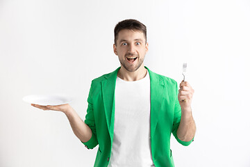 Image showing Young smiling attractive guy holding empty dish and fork isolated on grey background.