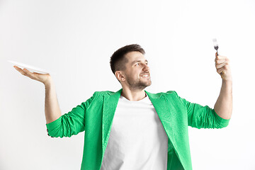 Image showing Young smiling attractive guy holding empty dish and fork isolated on grey background.