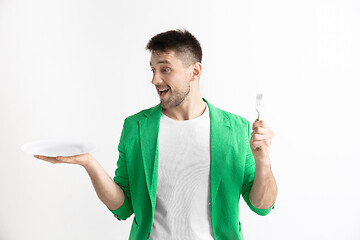 Image showing Young smiling attractive guy holding empty dish and fork isolated on grey background.