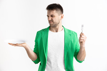 Image showing Young sad attractive guy holding empty dish and fork isolated on grey background.