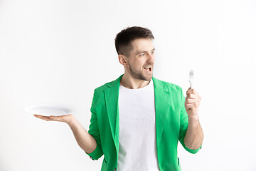 Image showing Young smiling attractive guy holding empty dish and fork isolated on grey background.
