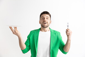 Image showing Young smiling attractive guy holding empty dish and fork isolated on grey background.