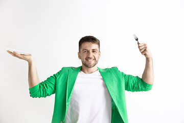 Image showing Young smiling attractive guy holding empty dish and fork isolated on grey background.