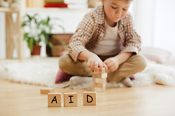 Image showing Wooden cubes with word AID in hands of little boy at home.