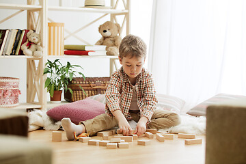 Image showing Little child sitting on the floor. Pretty boy palying with wooden cubes at home