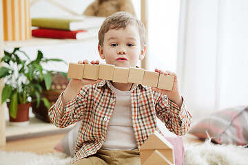 Image showing Little child sitting on the floor. Pretty boy palying with wooden cubes at home