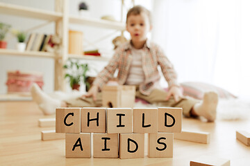 Image showing Wooden cubes with words CHILD AIDS in hands of little boy at home.