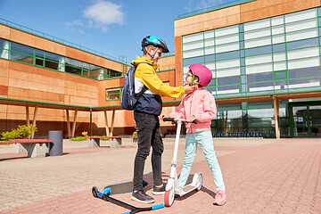 Image showing school boy fastening girl\'s helmet for scooter