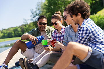 Image showing happy friends drinking tea from thermos in summer