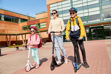 Image showing happy school children with mother riding scooters