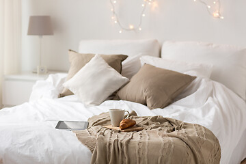 Image showing tablet pc, coffee cup and croissant on bed at home