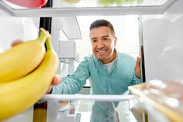 Image showing man taking banana from fridge at home kitchen