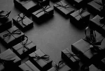 Image showing Arranged Gifts boxes wrapped in black paper with black ribbon on black background. Christmas concept