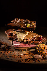 Image showing Stack of assorted chocolate with cocoa and cocoa beans on black background