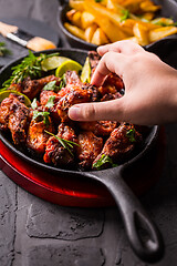 Image showing Hand swiping roasted chicken wings in barbecue sauce with lime 