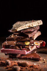 Image showing Stack of assorted chocolate with cocoa and cocoa beans on black background