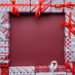 Image showing Arranged Gifts boxes wrapped in colorful festive paper with on burgund background