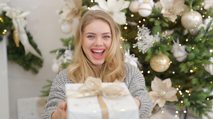 Image showing Smiling and happy young woman with christmas present box near christmas tree.