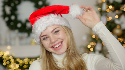 Image showing Young blond beautiful smiling woman in sweater and Santa hat on christmas tree background