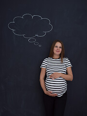 Image showing pregnant woman thinking in front of black chalkboard