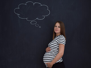 Image showing pregnant woman thinking in front of black chalkboard