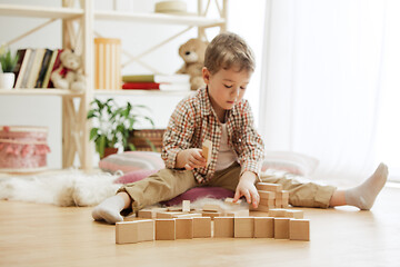 Image showing Little child sitting on the floor. Pretty boy palying with wooden cubes at home