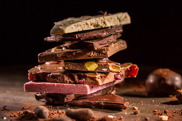 Image showing Stack of assorted chocolate with cocoa and cocoa beans on black background