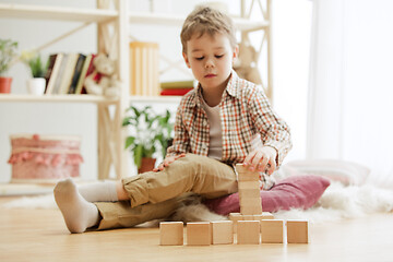 Image showing Little child sitting on the floor. Pretty boy palying with wooden cubes at home