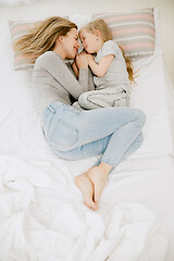 Image showing Young mother and her little daughter hugging and kissing on bed