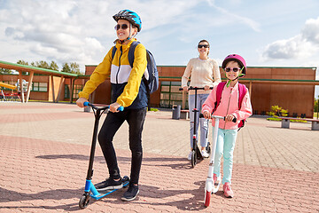 Image showing happy school children with mother riding scooters