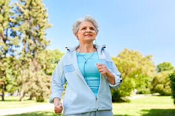 Image showing senior woman with earphones running in summer park