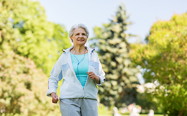 Image showing senior woman with earphones running in summer park