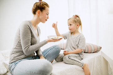 Image showing Young mother and her little daughter hugging and kissing on bed