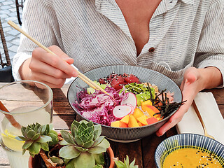 Image showing Woman eating tasty colorful healthy natural organic vegetarian Hawaiian poke bowl using asian chopsticks on rustic wooden table. Healthy natural organic eating concept