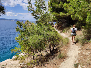 Image showing Young active feamle tourist wearing small backpack walking on coastal path among pine trees looking for remote cove to swim alone in peace on seaside in Croatia. Travel and adventure concept