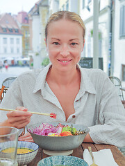 Image showing Woman eating tasty colorful healthy natural organic vegetarian Hawaiian poke bowl using asian chopsticks on rustic wooden table. Healthy natural organic eating concept