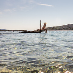 Image showing View of unrecognizable woman wearing big summer sun hat tanning topless and relaxing on old wooden pier in remote calm cove of Adriatic sea, Croatia