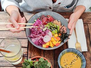 Image showing Woman eating tasty colorful healthy natural organic vegetarian Hawaiian poke bowl using asian chopsticks on rustic wooden table. Healthy natural organic eating concept