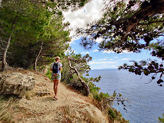 Image showing Young active feamle tourist wearing small backpack walking on coastal path among pine trees looking for remote cove to swim alone in peace on seaside in Croatia. Travel and adventure concept