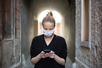 Image showing COVID-19 pandemic coronavirus. Casual caucasian woman at medieval city street using mobile phone, wearing protective face mask against spreading of coronavirus and disease transmission