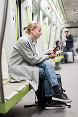 Image showing Portrait of lovely girl typing message on mobile phone in almost empty public subway train. Staying at home and social distancing recomented due to corona virus pandemic outbreak