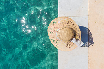 Image showing Woman wearing big summer sun hat relaxing on pier by clear turquoise sea.