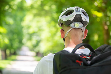 Image showing Rear view of unrecognizable man wearing protective helmet on bicycle cycling in city park