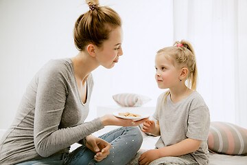 Image showing Young mother and her little daughter hugging and kissing on bed